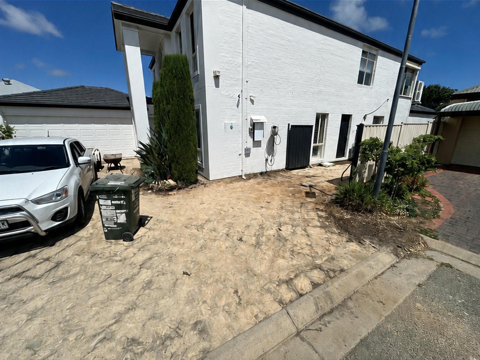 Front yard and driveway area cleared of pavers beside a white two-storey home