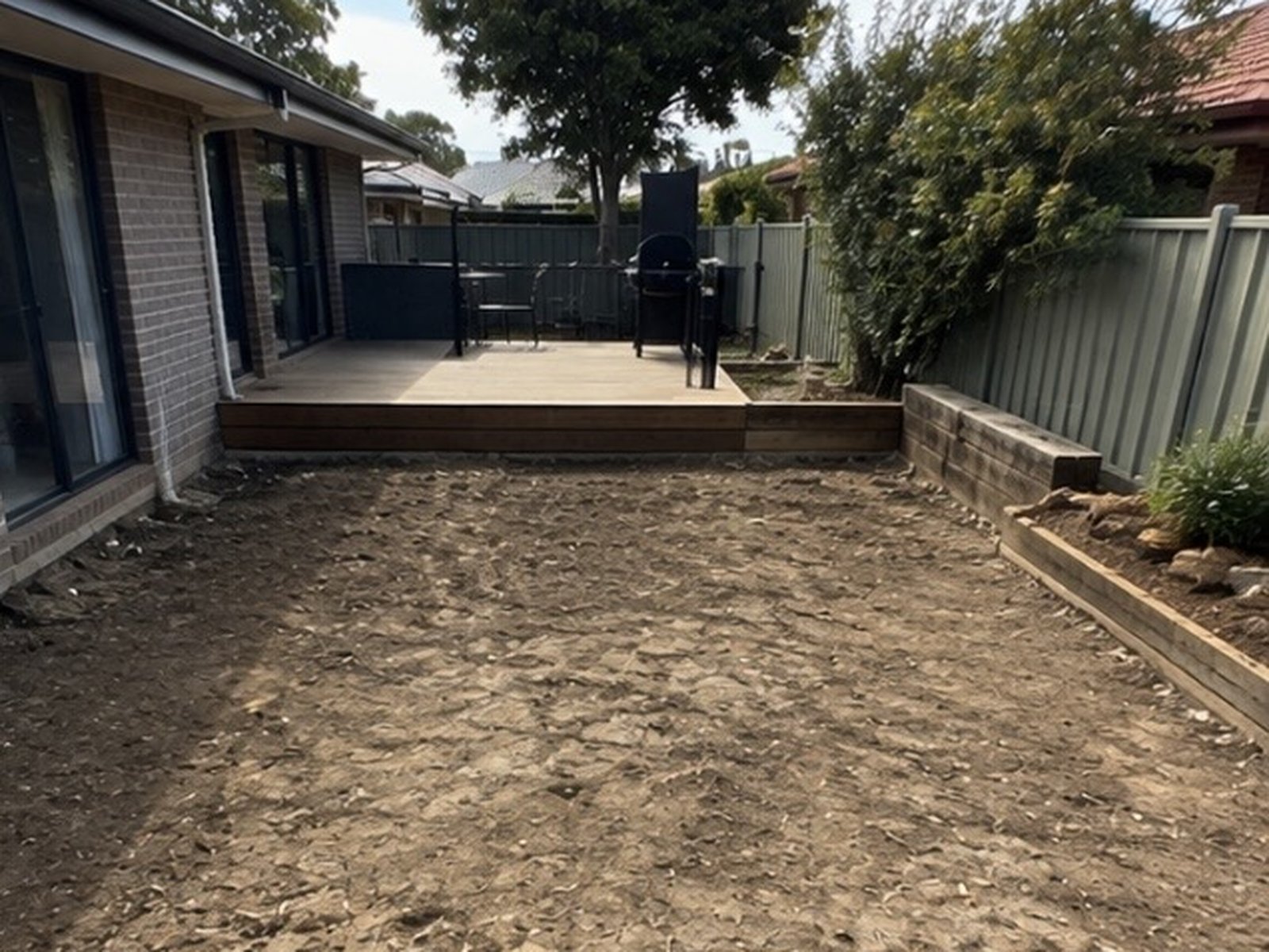 Backyard cleared of pavers back to bare soil beside a timber deck